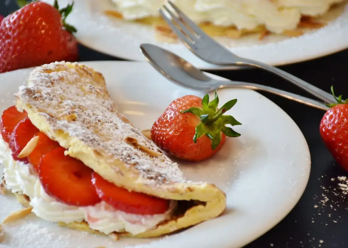Słodki omlet z truskawkami i bitą śmietaną, posypany cukrem pudrem. Idealny przepis na omlet na słodko.