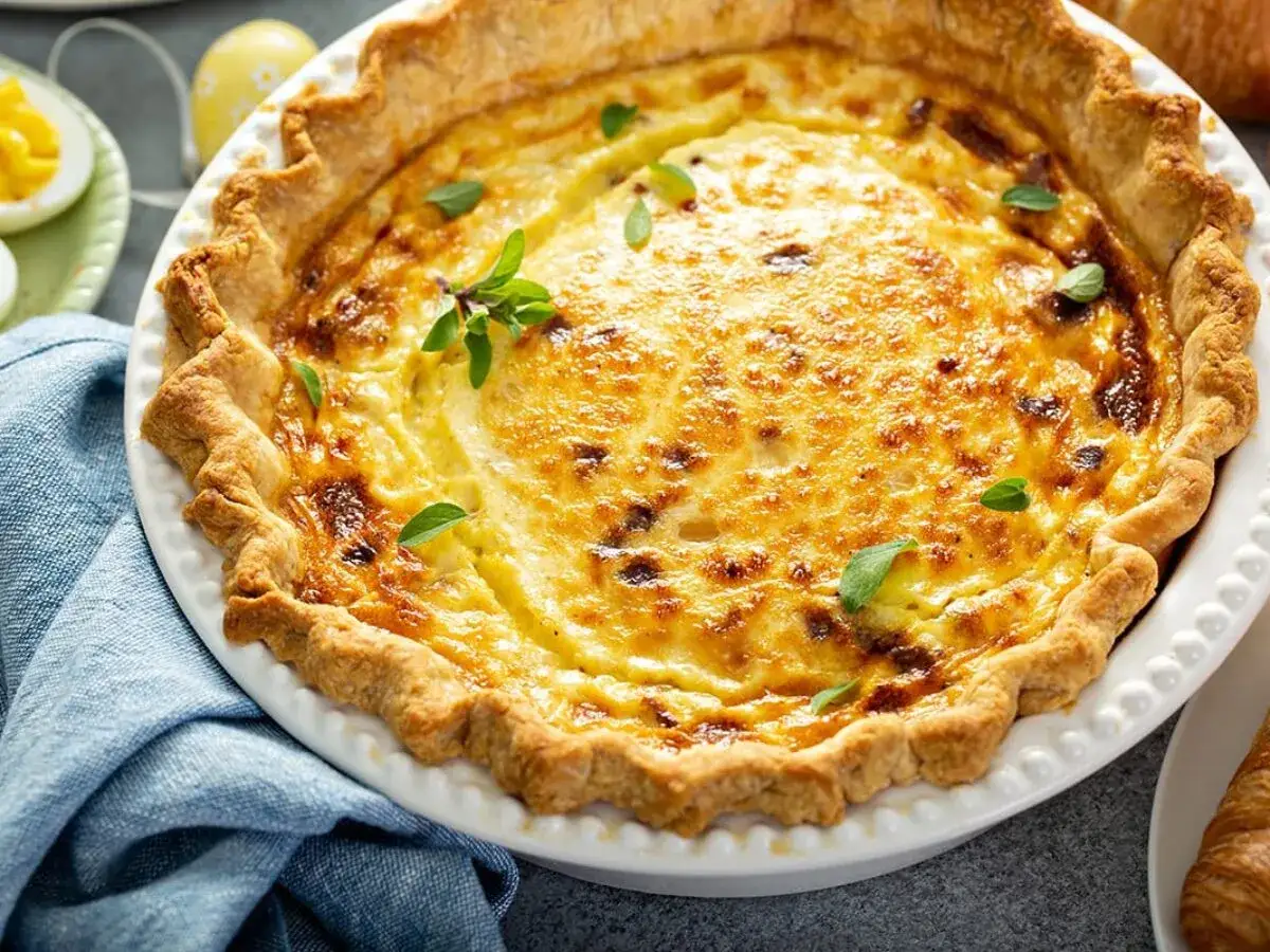 Une délicieuse quiche lorraine, un classique des plats lorrains, garnie de feuilles vertes.