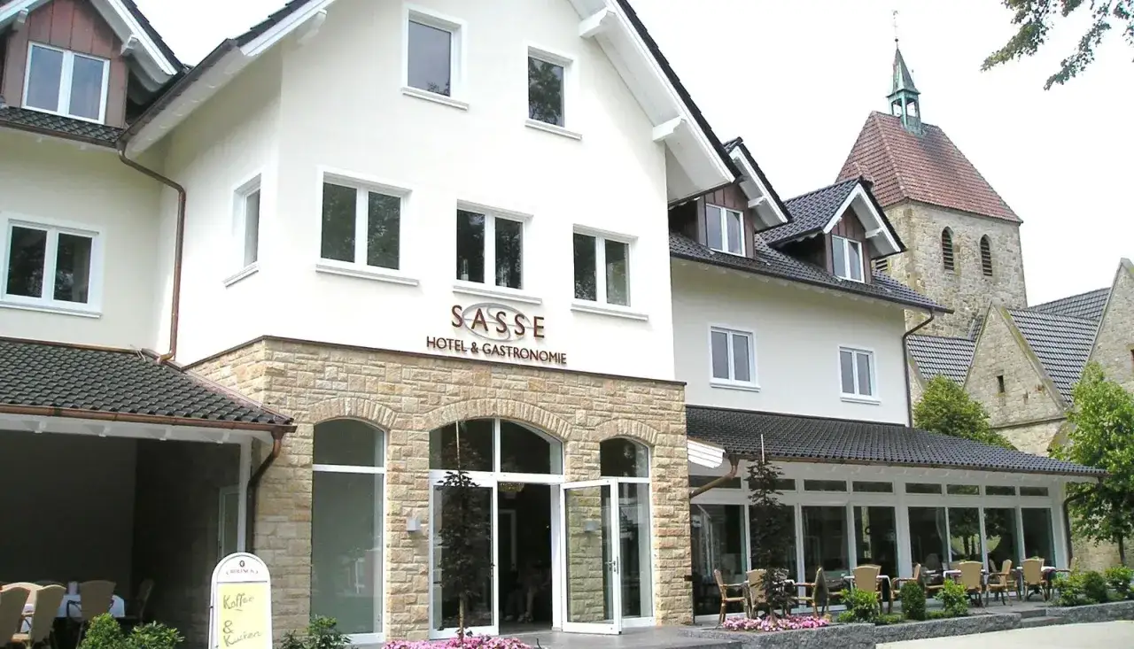 Gasthof Sasse in Soest mit Hotel & Gastronomie-Schild, Steinfassade und Kirche im Hintergrund.