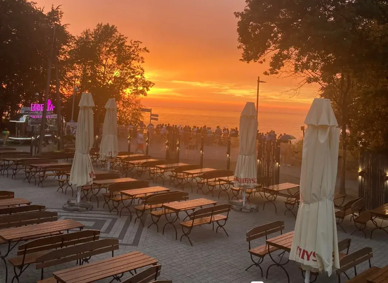 Zachód słońca nad morzem, z pustymi stolikami i ławkami w ogródku restauracji na klifie. Idealne miejsce na rybę i mięso po dniu pełnym wrażeń.
