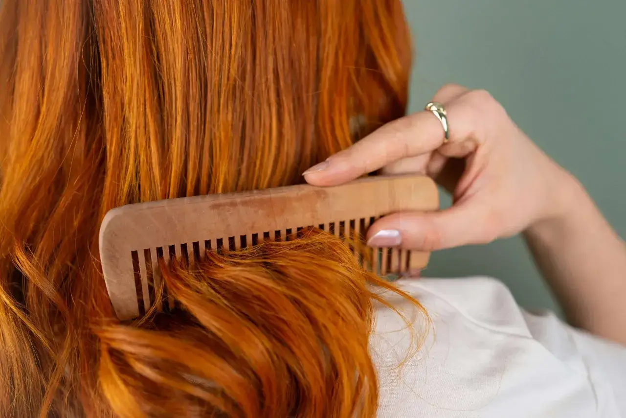 Mujer peina su cabello pelirrojo con un peine de madera. ¿En qué época del año se cae más el pelo? El otoño es conocido por ser el momento en que el cabello se cae más.