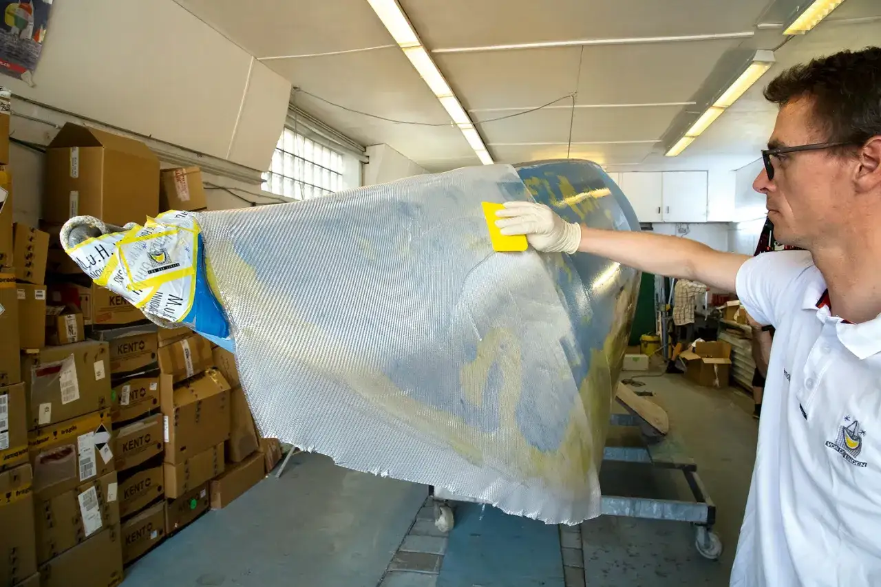Mann bearbeitet mit gelbem Werkzeug und Handschuh ein Bootsteil. Epoxidharz Bootsbau-Material wird aufgetragen.