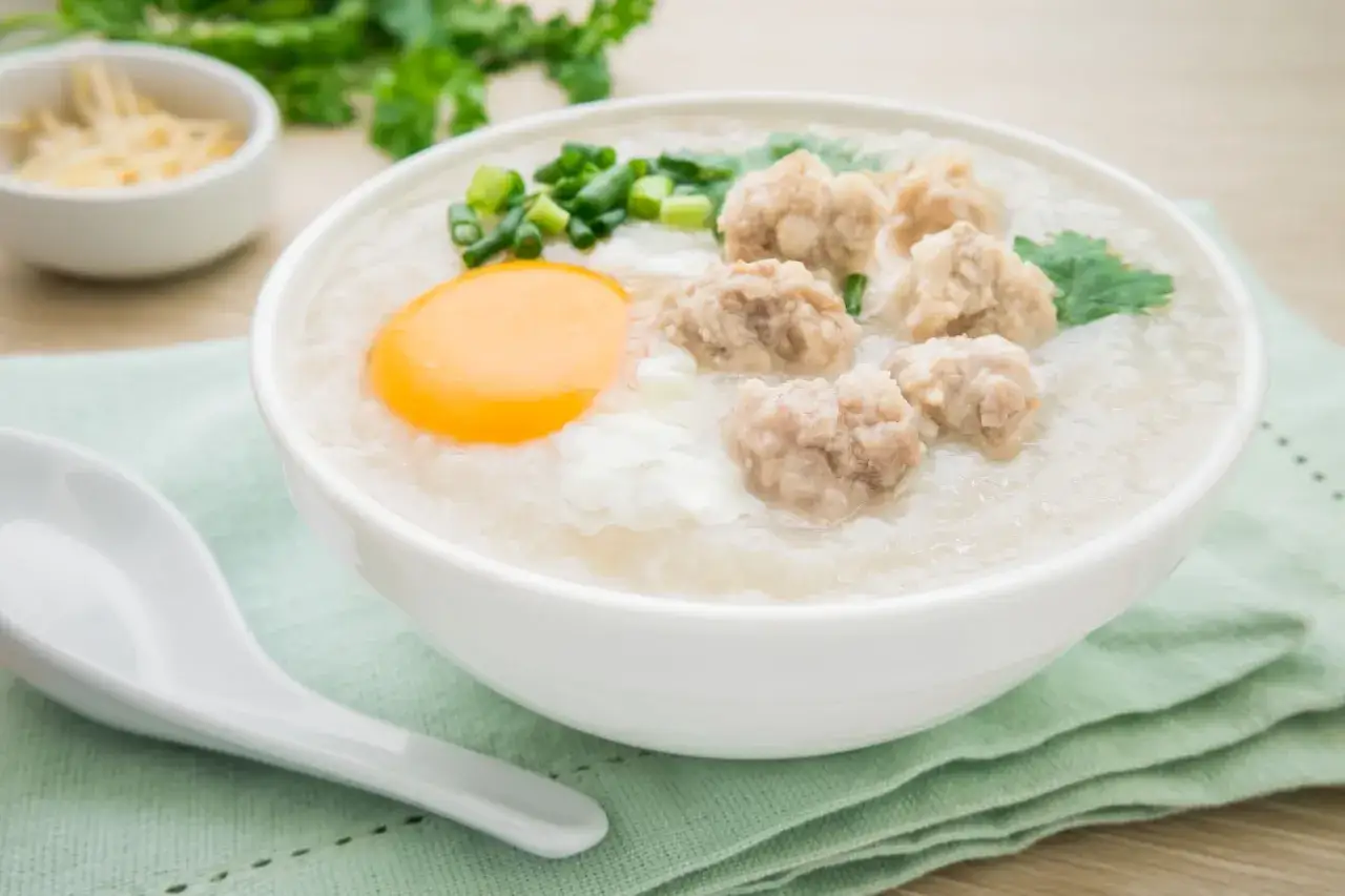 Miseczka aromatycznego congee z mięsnymi klopsikami, jajkiem i szczypiorkiem.