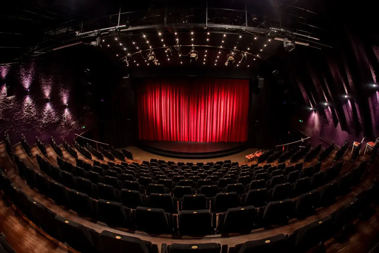 Pusta sala teatralna z czerwonymi kurtynami i rzędami czarnych foteli. Czekamy na spektakl z repertuaru Teatru Janda.