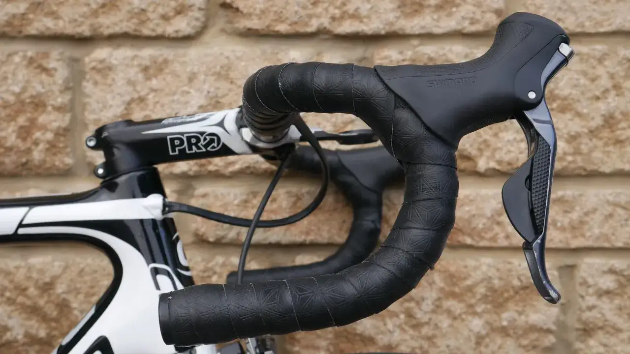 Czarna owijka na kierownicę roweru szosowego z subtelnym wzorem. Widoczna manetka Shimano i mostek PRO.