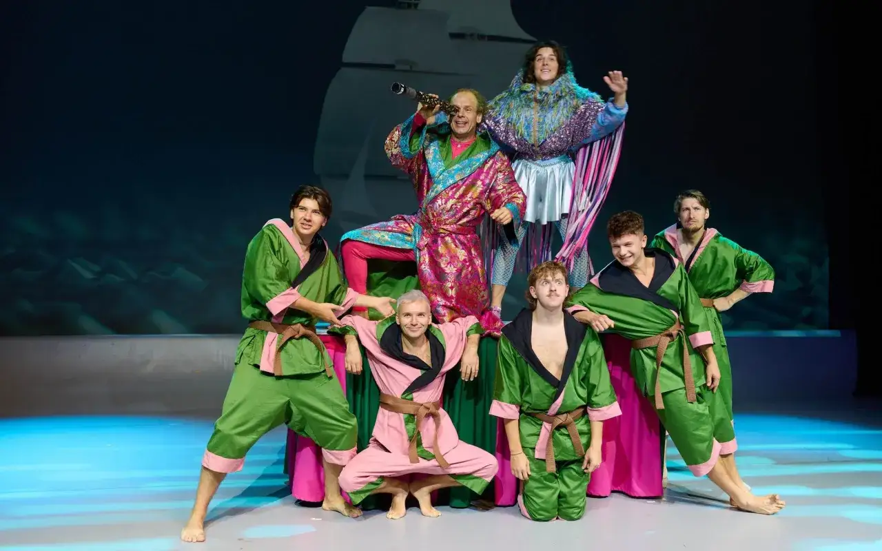 Aktorzy w barwnych strojach na scenie, przygotowujący się do spektaklu "Akademia Pana Kleksa teatr".