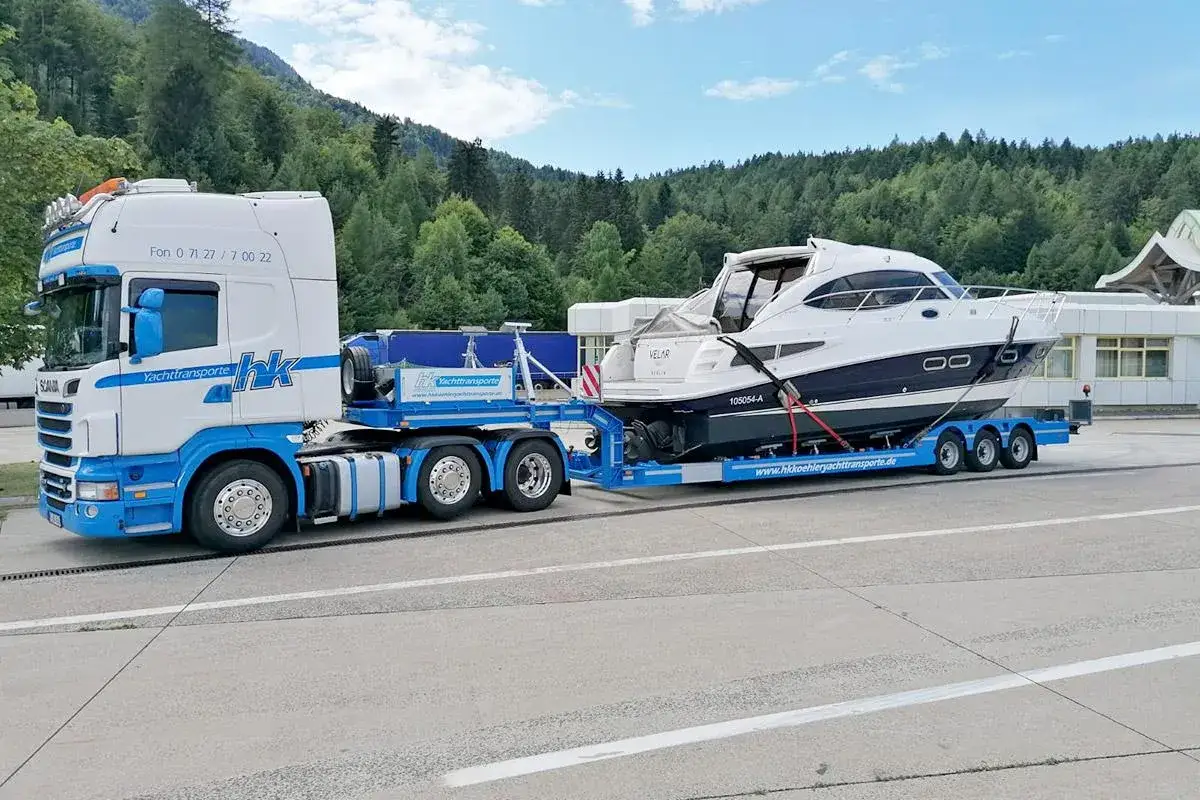 Ein LKW transportiert eine weiße Yacht auf einem Tieflader. Informieren Sie sich über bootstransport kosten für Ihre nächste Überführung.