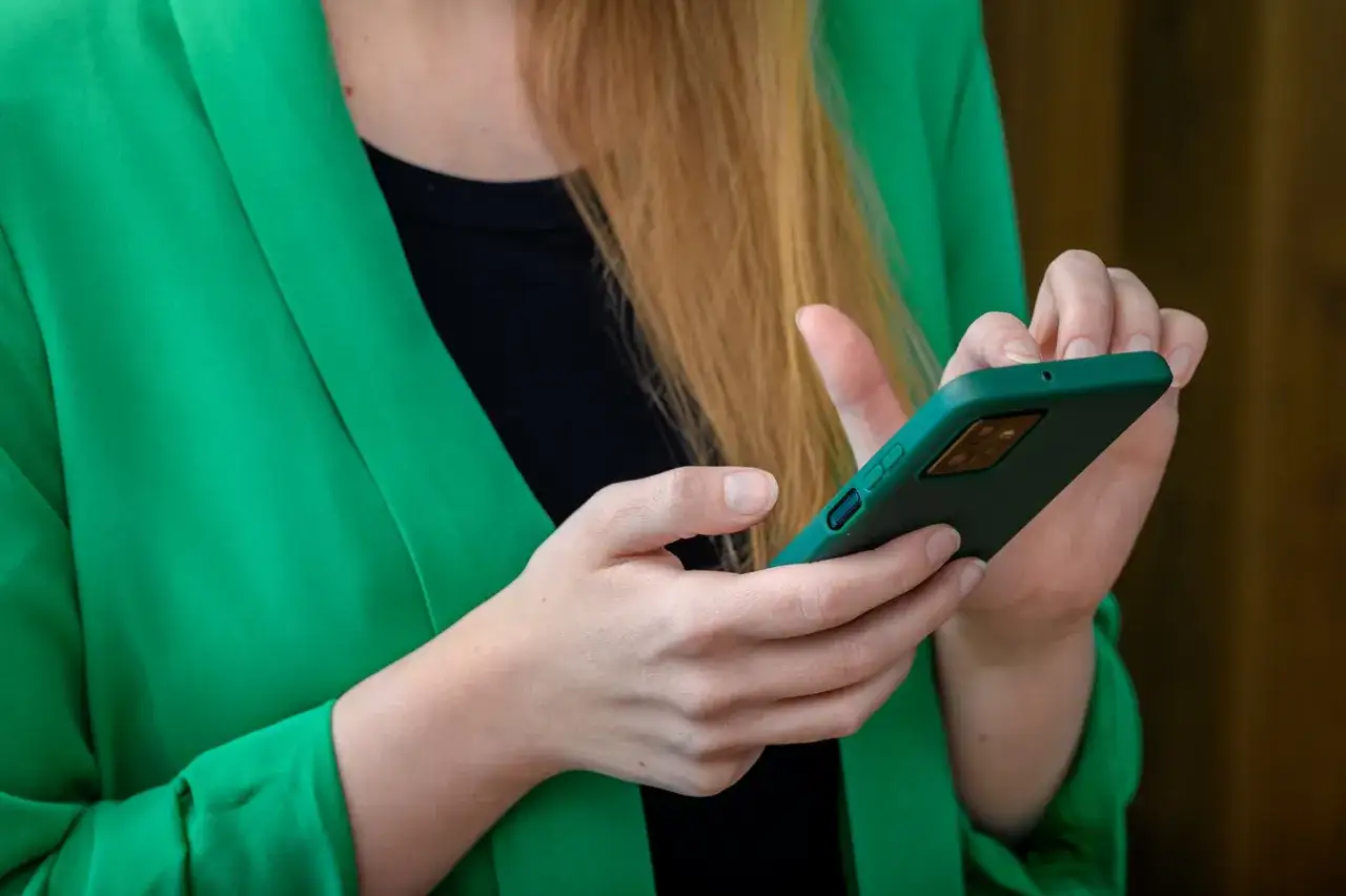 Kobieta w zielonej marynarce trzyma smartfon. Szuka informacji, gdzie jest schowek w telefonie Samsung, aby zabezpieczyć swoje dane.