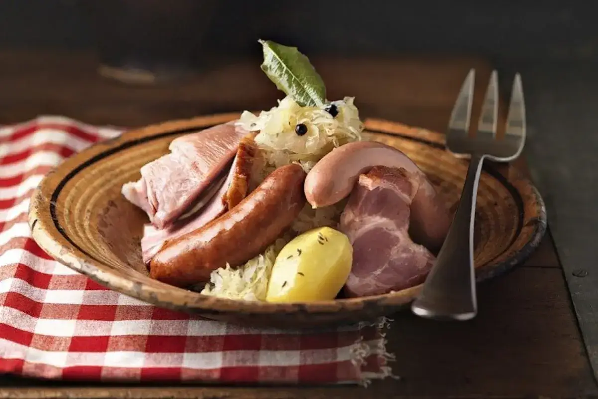 Assiette de choucroute garnie, évoquant son origine alsacienne, avec saucisses, lard, jambon et pommes de terre.