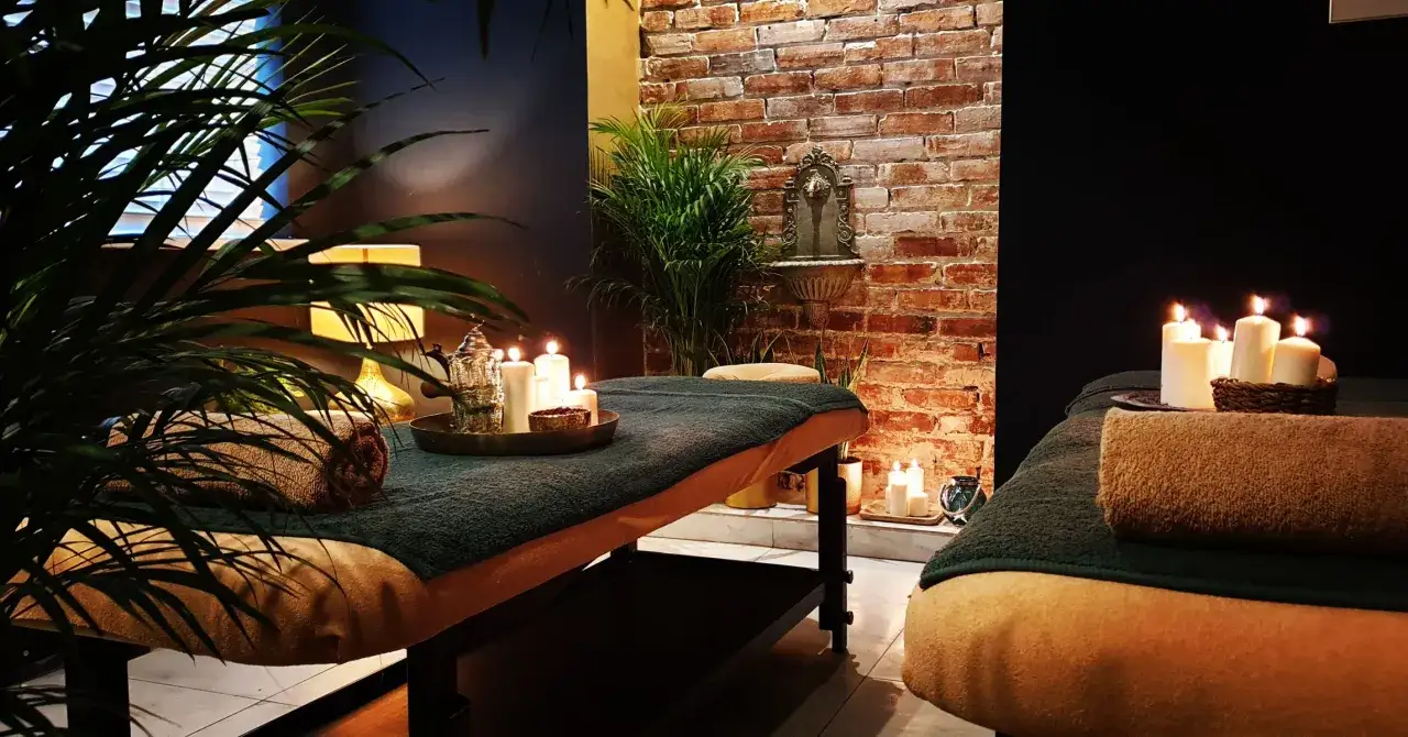 Dwie łóżka do masażu w przytulnym spa, ozdobione świecami i roślinami.