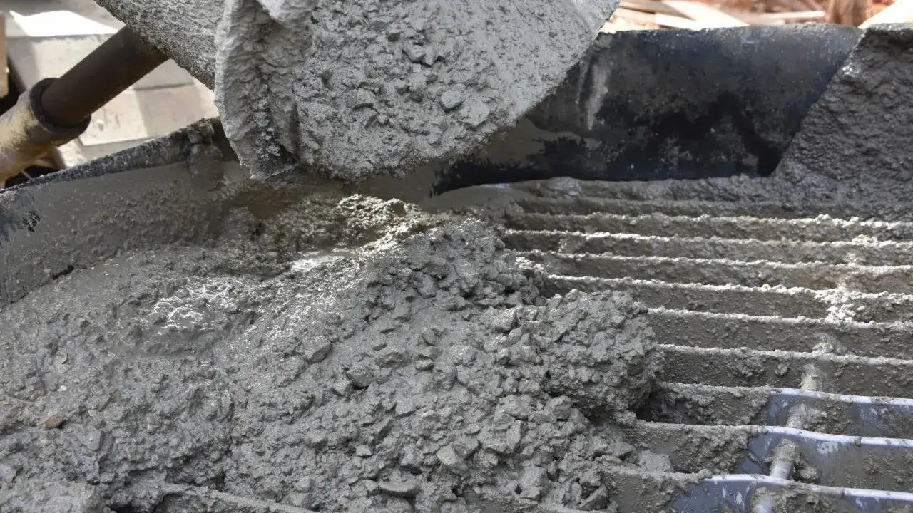 Świeży beton z kruszywem, idealny jako jaki beton pod obrzeża, wylewany z maszyny na ruszt.