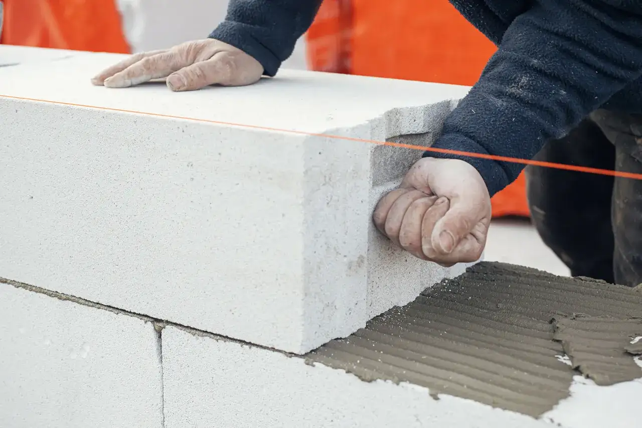 Ręce budowlańca podczas murowania ścianek działowych z bloczków betonowych. Widać zaprawę i sznur murarski.
