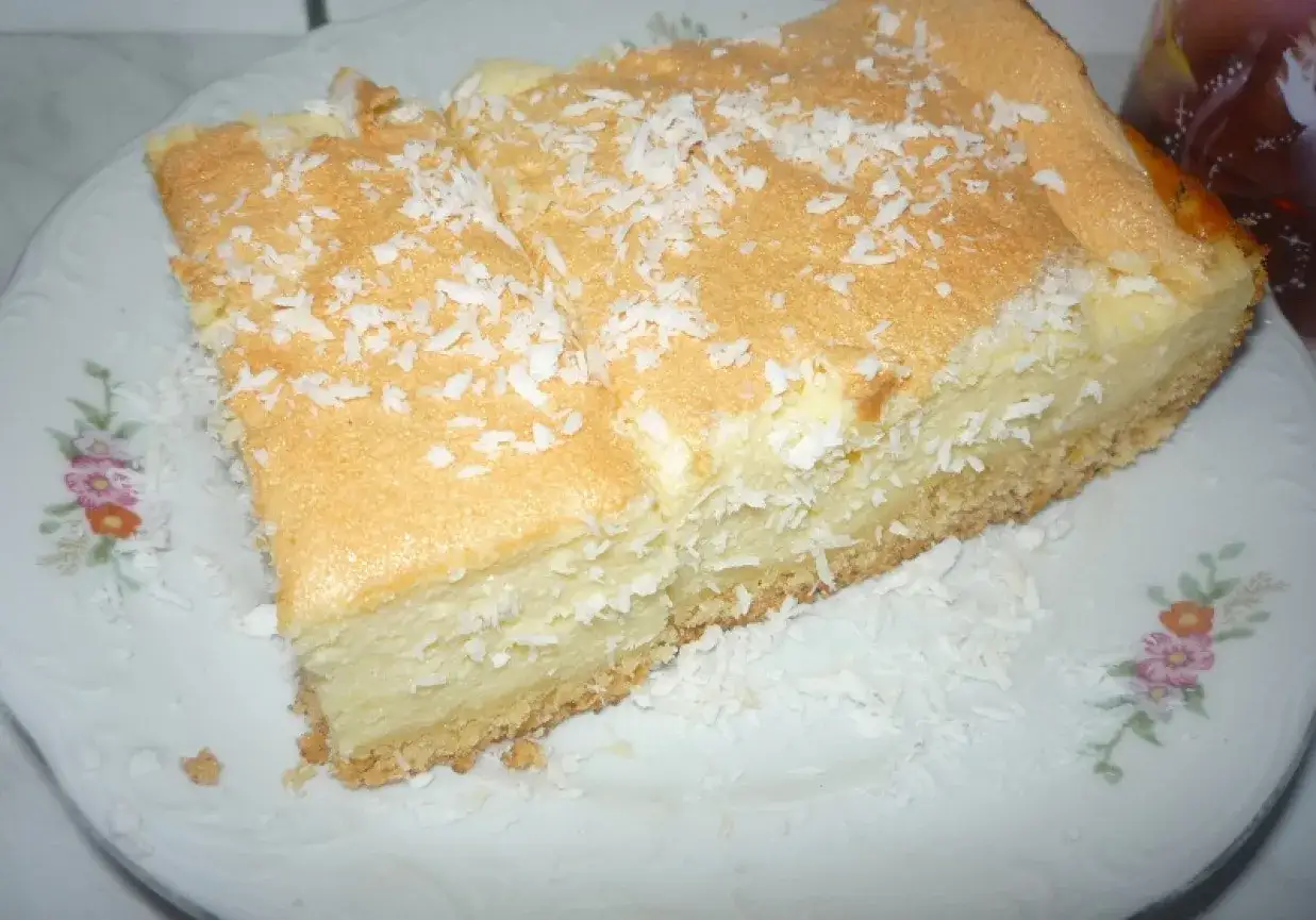 Pyszny sernik z wiórkami kokosowymi na wierzchu, podany na talerzu z kwiatowym wzorem.