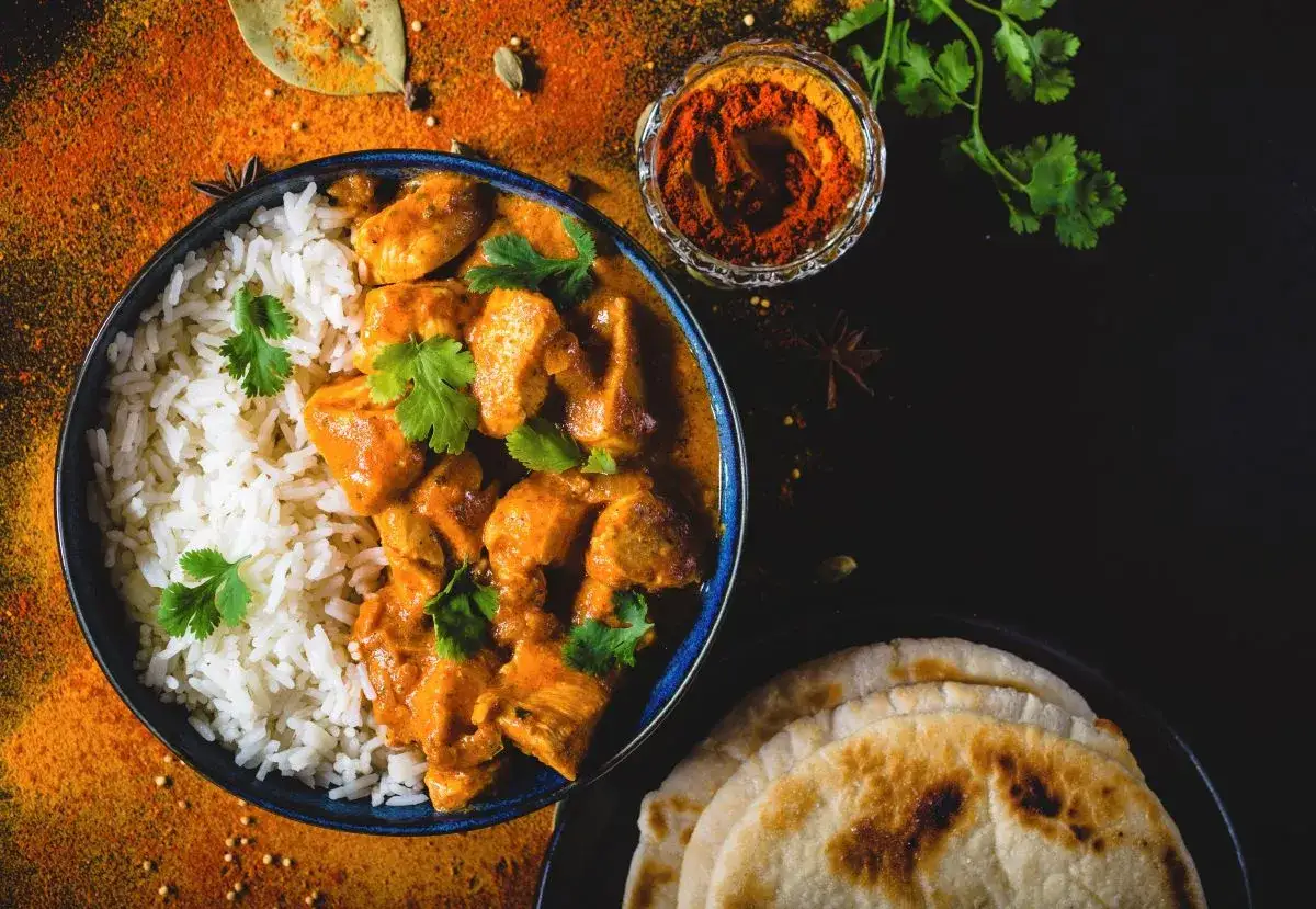 Pyszny Butter Chicken przepis: kremowy kurczak w sosie pomidorowym z ryżem i plackami naan, ozdobiony świeżą kolendrą i przyprawami.