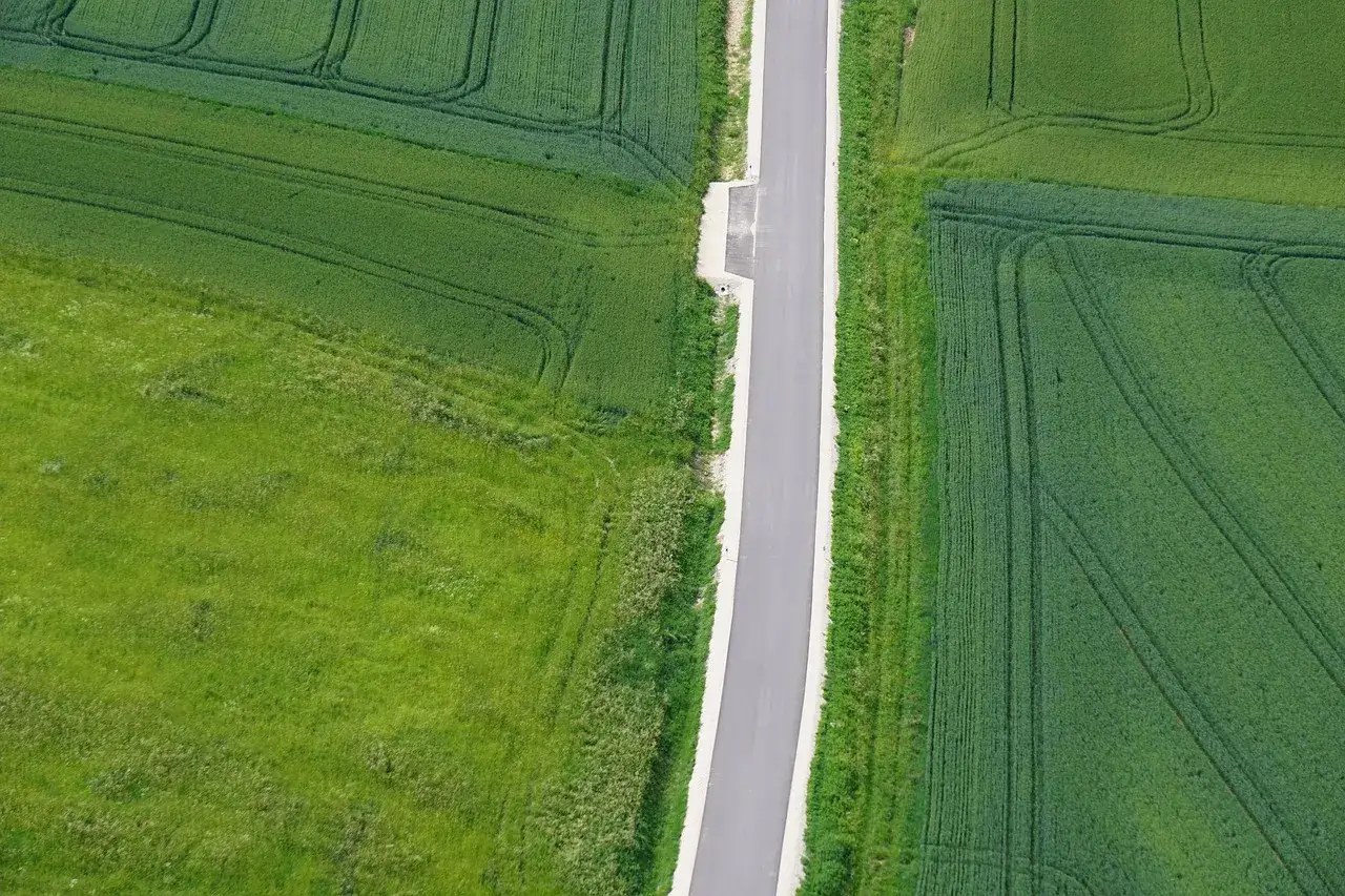 Asfaltowa droga wewnętrzna przecina zielone pola uprawne.