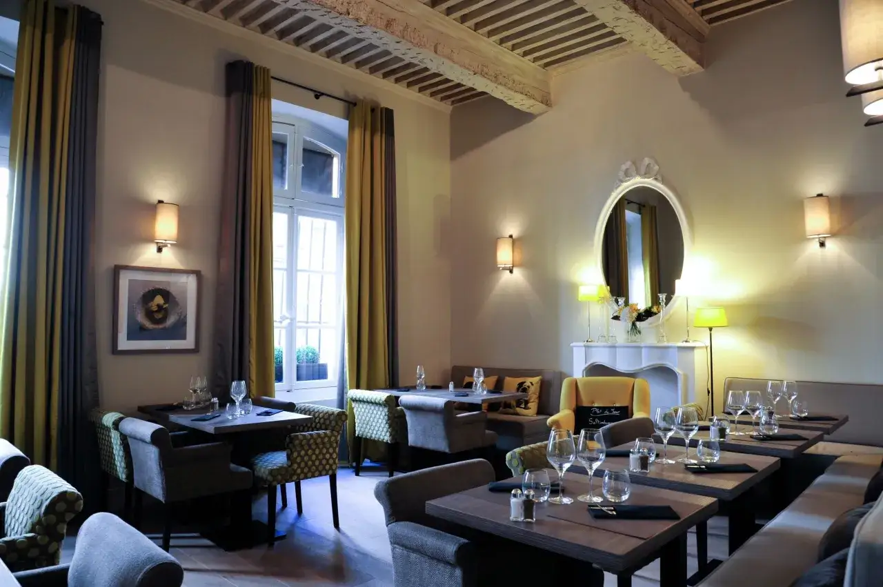 Salle à manger élégante avec tables dressées, fauteuils confortables et un miroir orné. L'ambiance évoque une **spécialité provençale** raffinée.