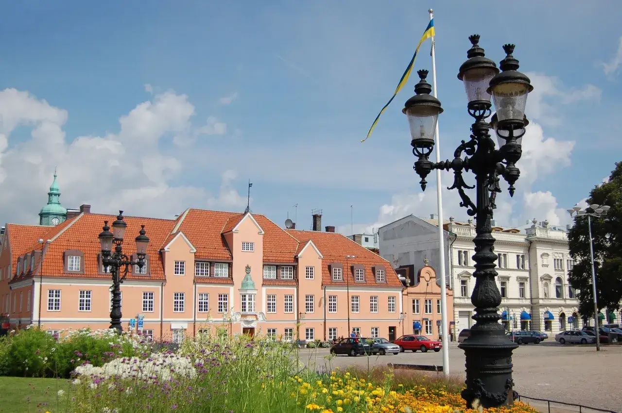 Blumen blühen am Karlskrona Hafen. Ein prächtiges Gebäude mit orangem Dach und eine schwedische Flagge im Wind.