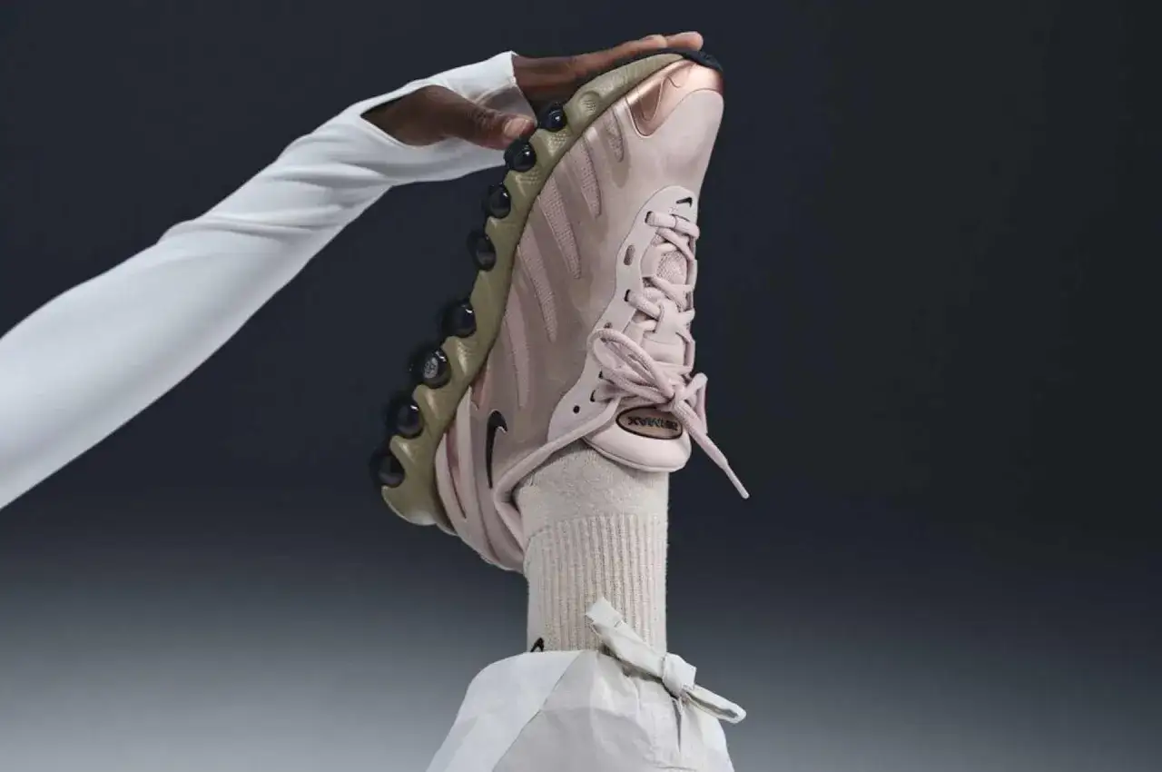 Różowy but Nike na obcasie, trzymany przez dłoń w białej rękawiczce.