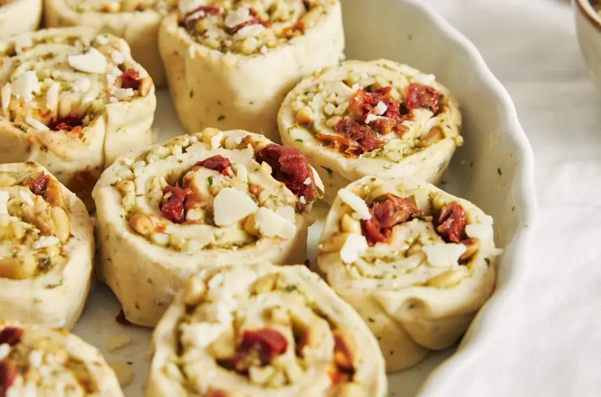 Roladki z ciasta do pizzy z suszonymi pomidorami, orzeszkami pinii i parmezanem, gotowe do pieczenia.