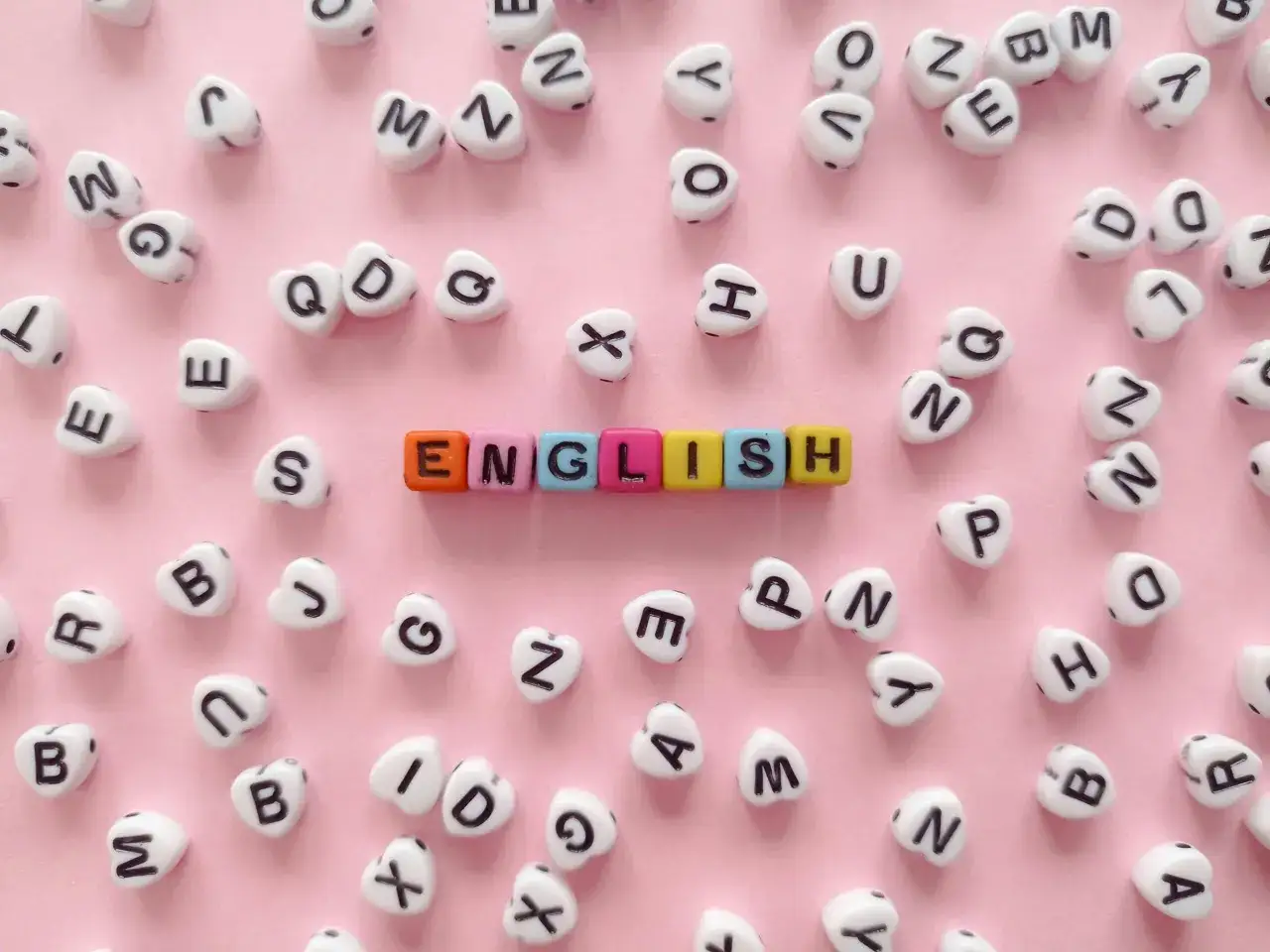 Kolorowe koraliki z literami tworzą napis "ENGLISH" na różowym tle.