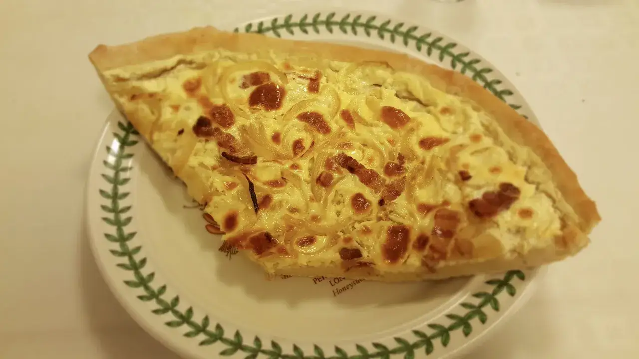 Part de quiche lorraine, une des spécialités lorraines, sur une assiette décorée de feuilles vertes.