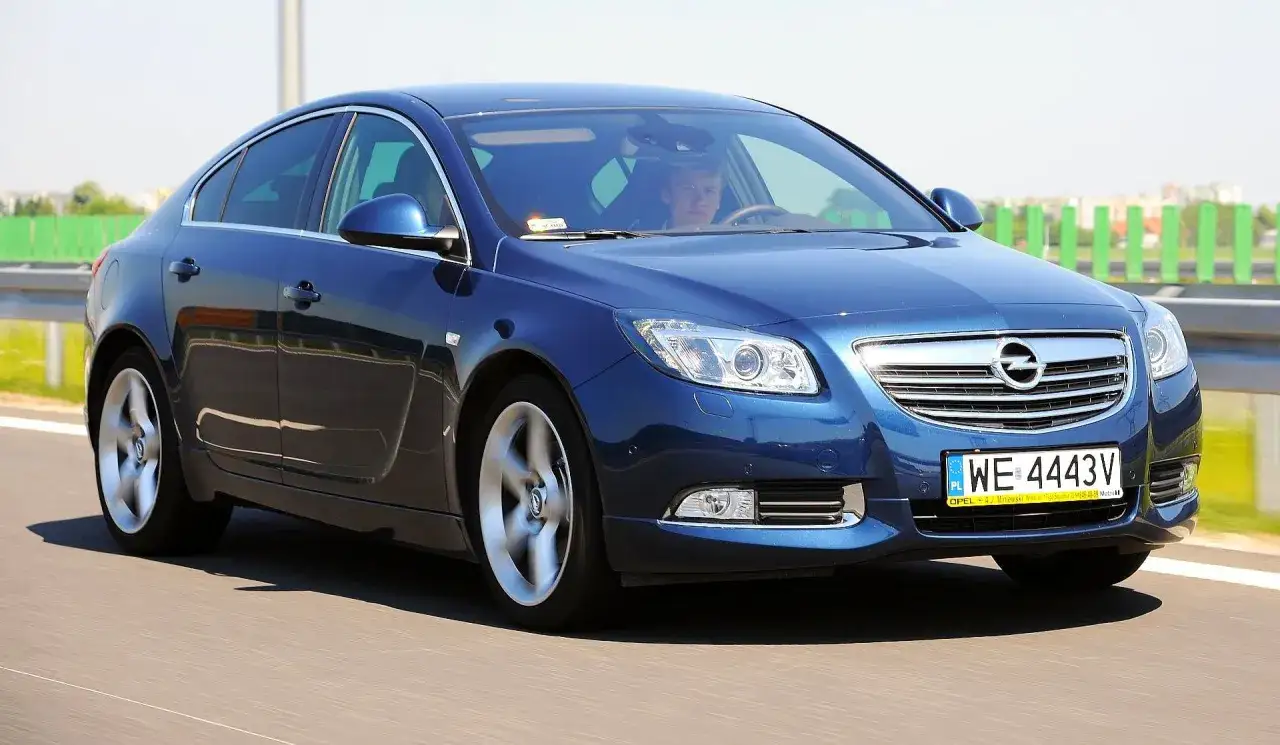 Niebieski Opel Insignia 2.0 CDTI w ruchu drogowym. Kierowca za kierownicą.