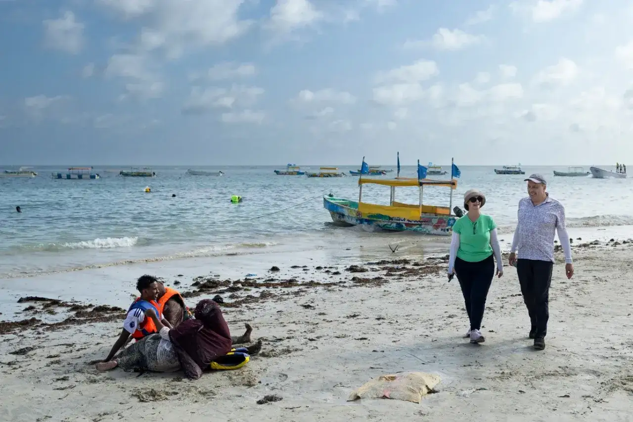 Spacerowery na plaży w Somalii, z łodziami na morzu. Czy Somalia jest bezpieczna? Turyści spacerują, podczas gdy lokalni mieszkańcy odpoczywają na piasku.