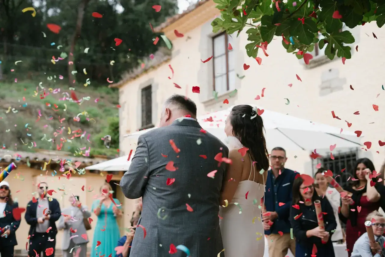 Novios bajo una lluvia de confeti en forma de corazón. Los invitados lanzan confeti, creando un ambiente festivo, perfecto para las canciones de boda.