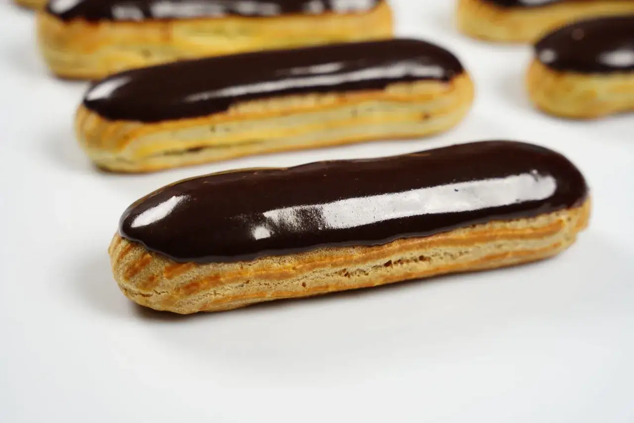 Plusieurs éclairs au chocolat brillants, avec un fondant pour éclair parfait, sont disposés sur fond blanc.