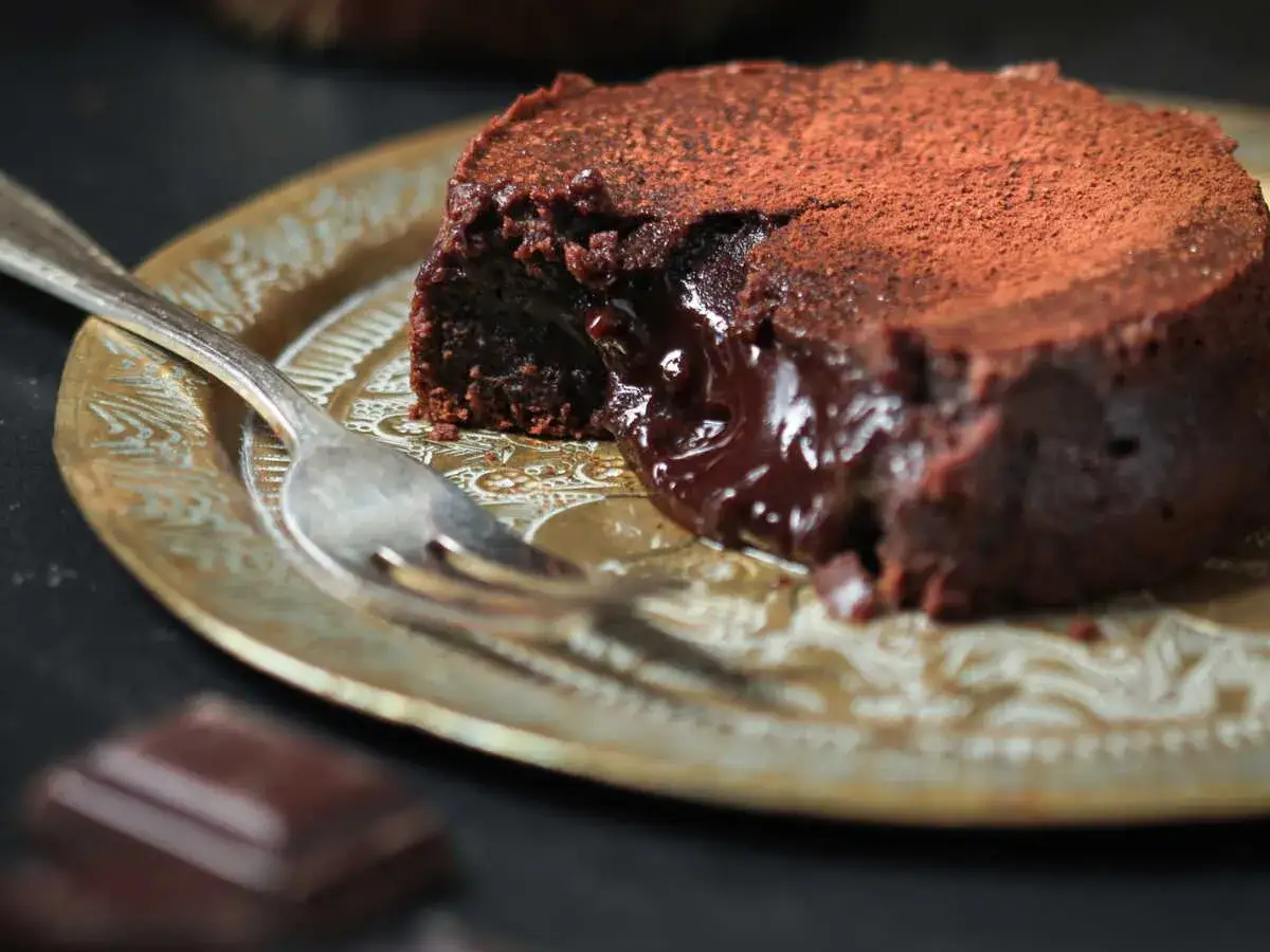 Fondant au chocolat cacao, cœur coulant, saupoudré de cacao, sur une assiette dorée avec une fourchette.