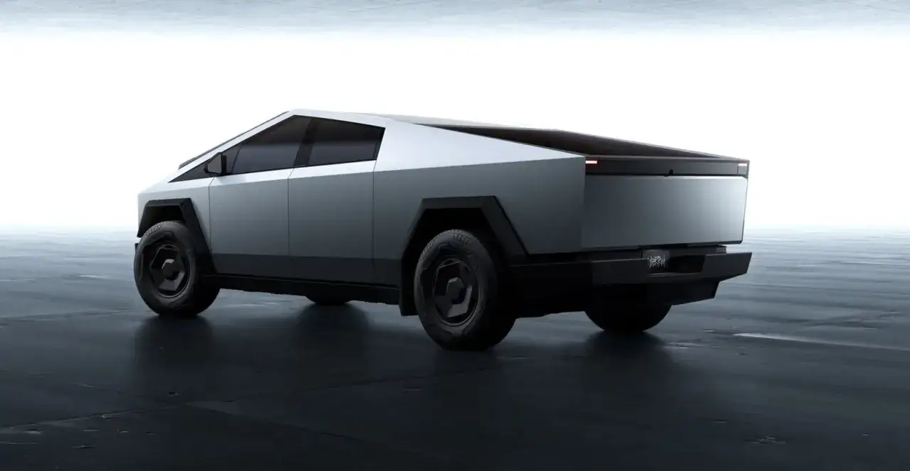 Futurystyczny Tesla Cybertruck w kolorze srebrnym, z ostrymi krawędziami i masywnymi kołami, prezentuje się na ciemnej, betonowej podłodze.