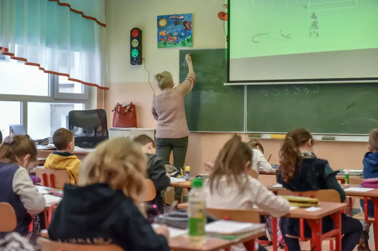 Nauczycielka dyplomowana pisze na tablicy, dzieci słuchają. Ciekawe, jakie nauczyciel dyplomowany zarobki ma w tej szkole.