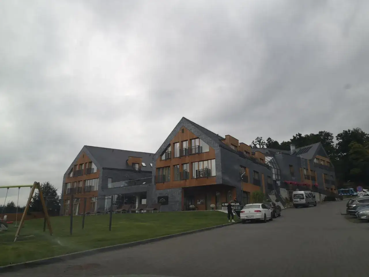 Nowoczesny hotel z drewnianymi elementami i kamienną elewacją. Na trawniku plac zabaw. Wiele pozytywnych osada-sniezka opinie potwierdza jego urok.