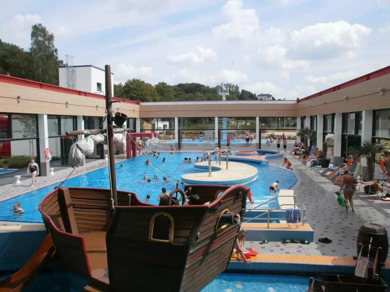 Ein Piratenschiff-Spielplatz in einem Freibad mit vielen Badegästen.