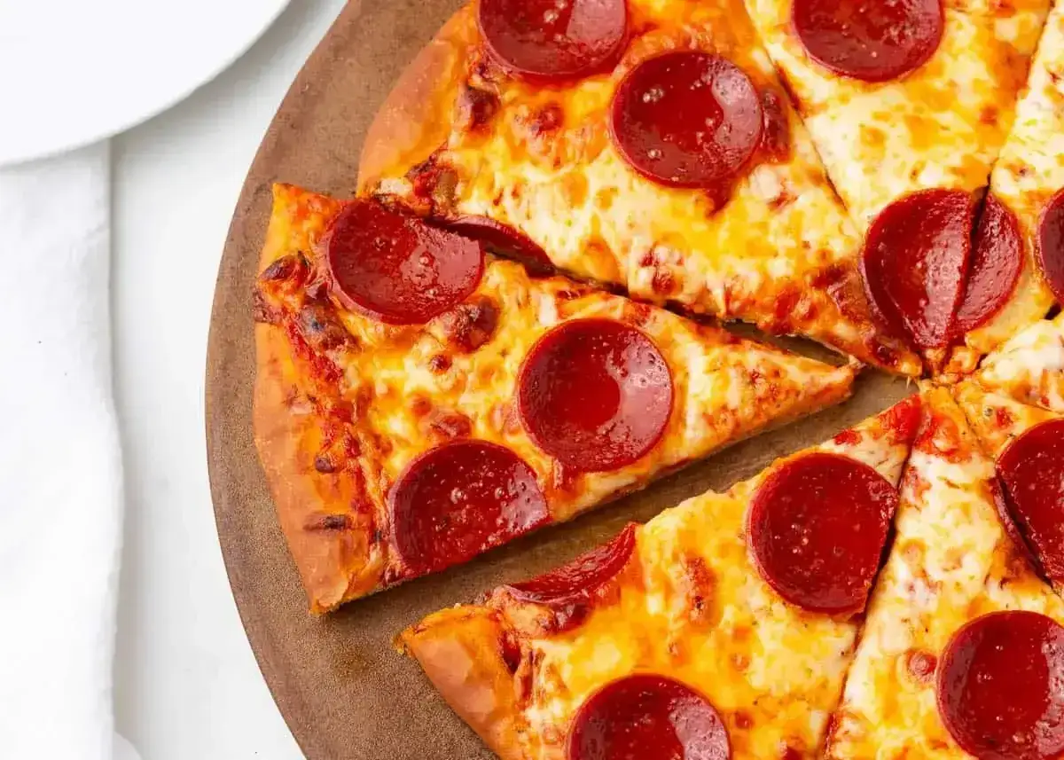Kawałki pizzy z serem i okrągłymi plasterkami peperoni, ułożone na drewnianej desce.