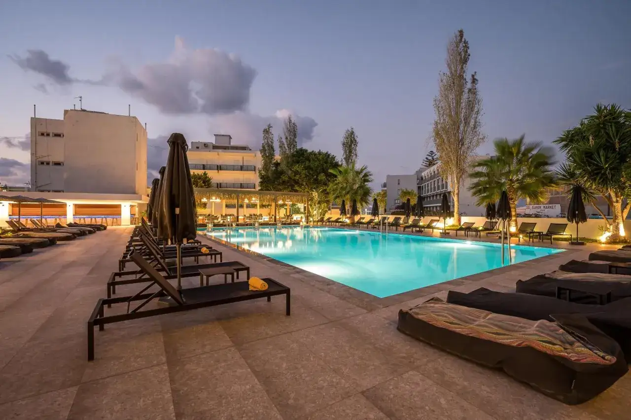 Basen hotelowy oświetlony nocą, leżaki i palmy. Idealne miejsce na relaks, zgodnie z licznymi heronissos hotel opinie.