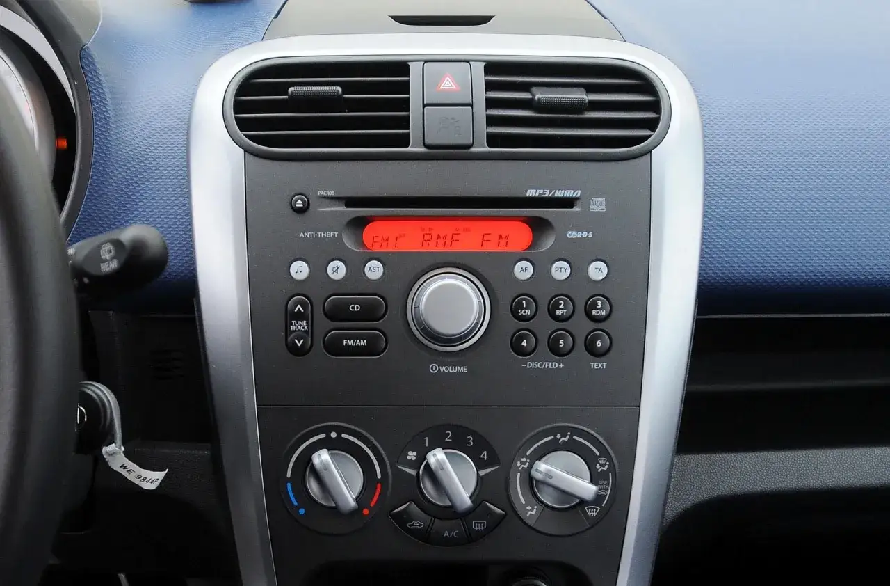 Panel radia i klimatyzacji w Oplu Agila. Czerwony wyświetlacz radia pokazuje "FM1 RMF FM".