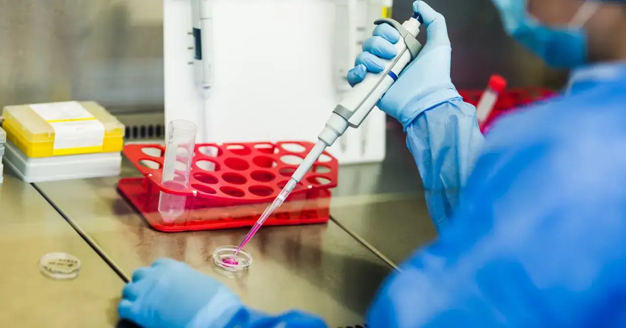 Naukowczyni w niebieskim fartuchu pobiera pipetą próbkę, która może być cenną **krwią pępowinową**, do dalszych badań laboratoryjnych.