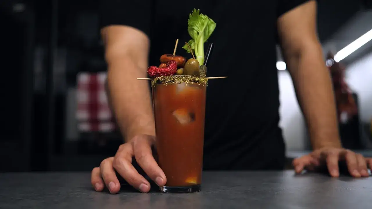 Bloody Mary na soku pomidorowym kontra na passacie. W szklance drink z lodem, ozdobiony oliwkami, suszonym pomidorem, kiełbaską i selerem.