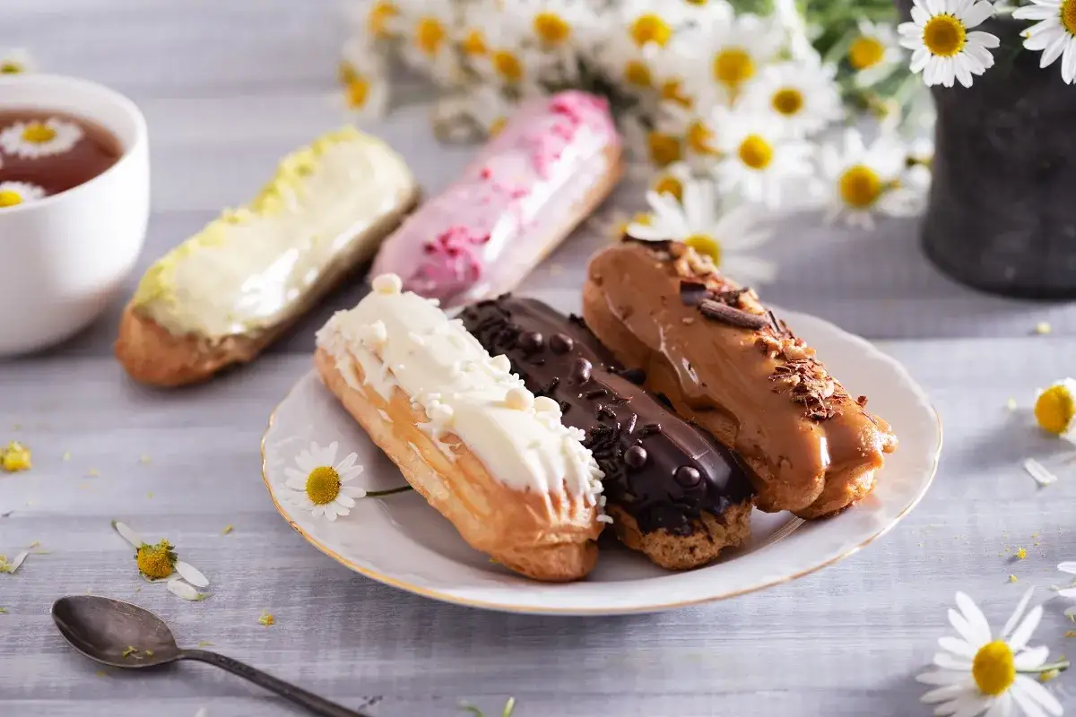 Eklery z czekoladą i profiteroles, ozdobione kwiatami, kuszą smakiem. Idealne na popołudniową herbatę.