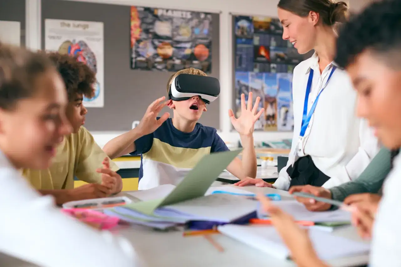 Chłopiec w goglach VR przeżywa lekcję, a nauczycielka z uśmiechem obserwuje tę innowację pedagogiczną.