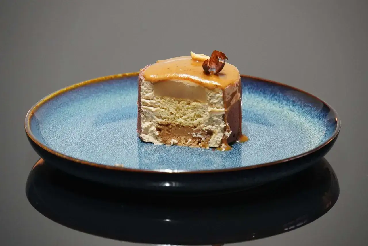 Tranche d'entremet aux couches aériennes, surmontée d'un glaçage caramel et d'une noisette croquante. Le biscuit noisette pour entremet offre une texture légère et savoureuse.