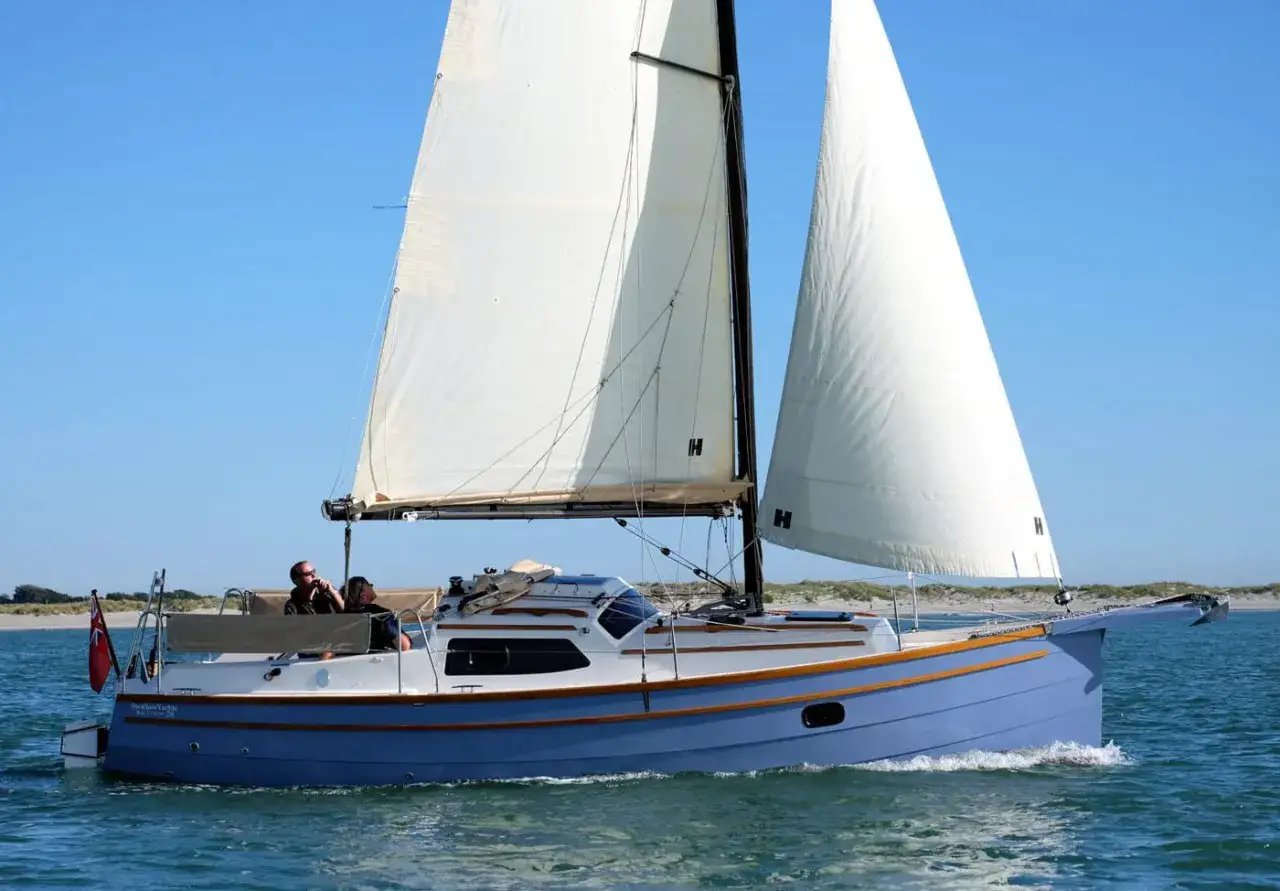 Eine blaue Baycruiser 26 segelt auf ruhigem Wasser unter klarem Himmel. Zwei Personen genießen die Fahrt.