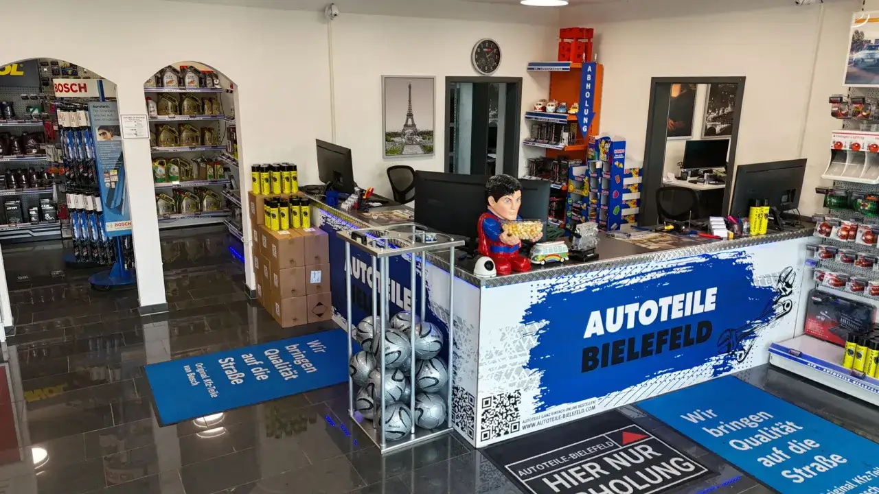 Autoteile-Shop mit Theke, Regalen voller Autoteile, einem Superman-Aufsteller und Fußmatten.