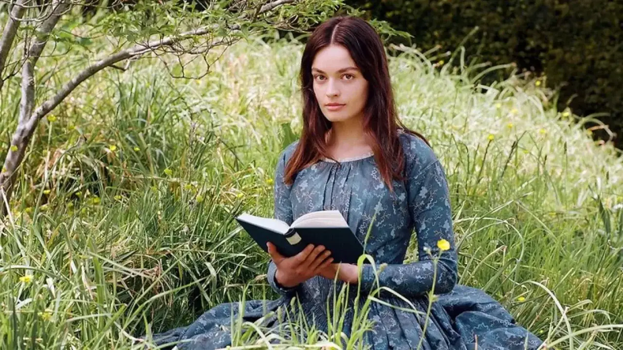 Młoda kobieta w sukni z epoki, czytająca książkę na łące, symbolizuje, jak ewoluowała postać kobieca w powieściach Jane Austen i sióstr Brontë.