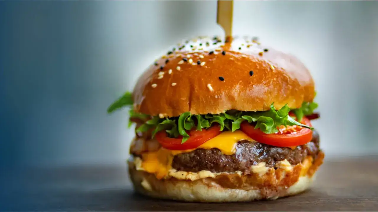Un délicieux burger, avec sa brioche dorée, sa viande juteuse, son fromage fondant, sa laitue croquante et ses tomates fraîches. On se demande d'où vient le burger, ce classique indémodable.