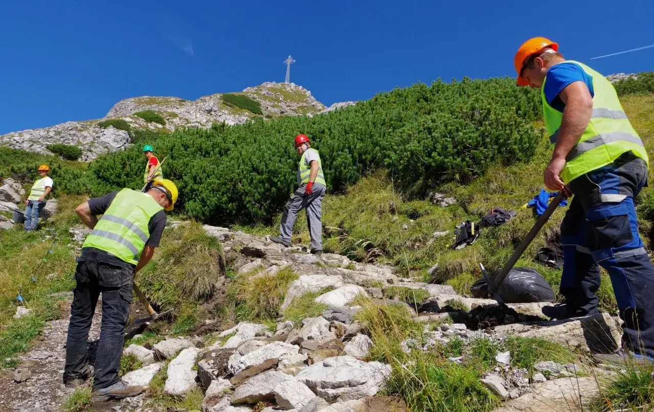 Pracownicy konserwują szlak na Giewont. Czy szlak na Giewont jest trudny? Widać krzyż na szczycie, a teren jest kamienisty.