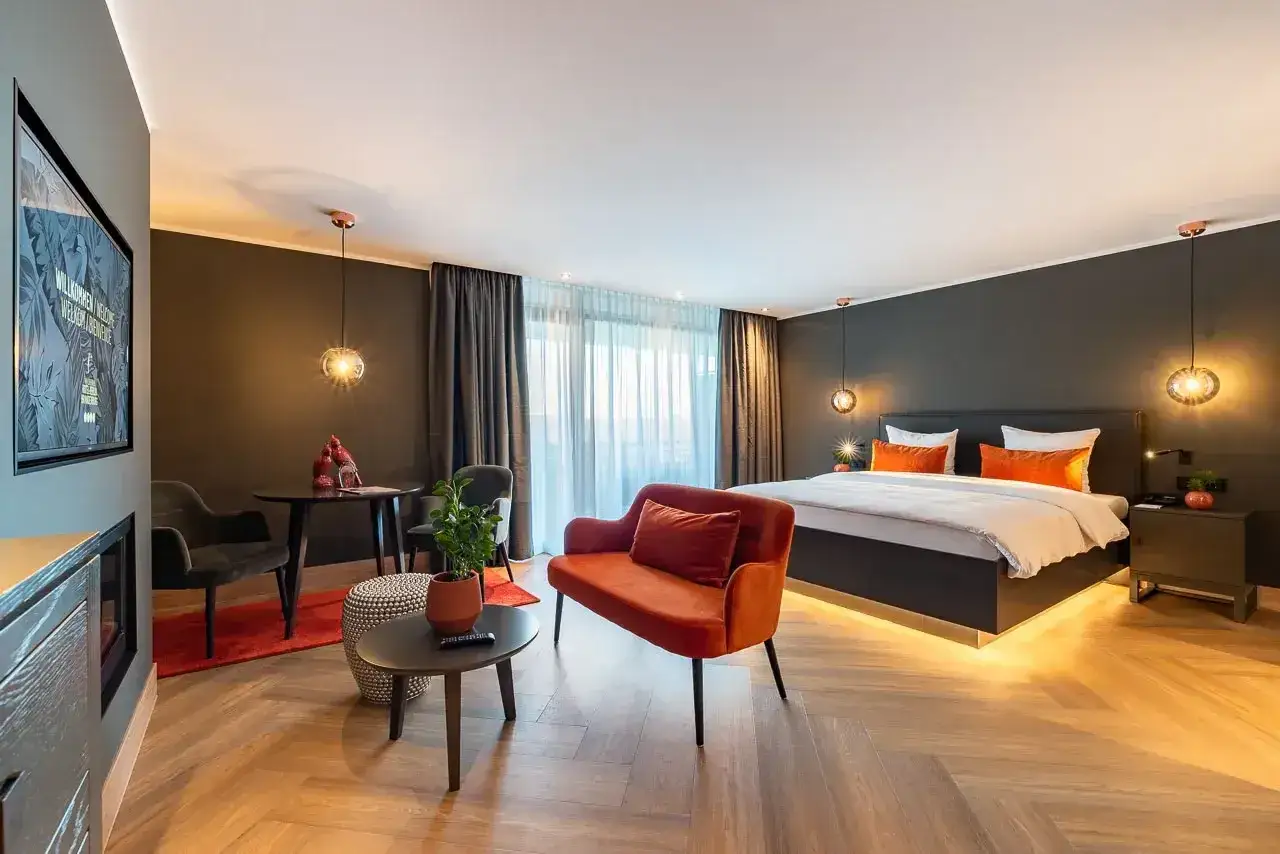 Modern Hotelzimmer mit großem Bett, orangefarbenem Sofa und Sitzbereich.