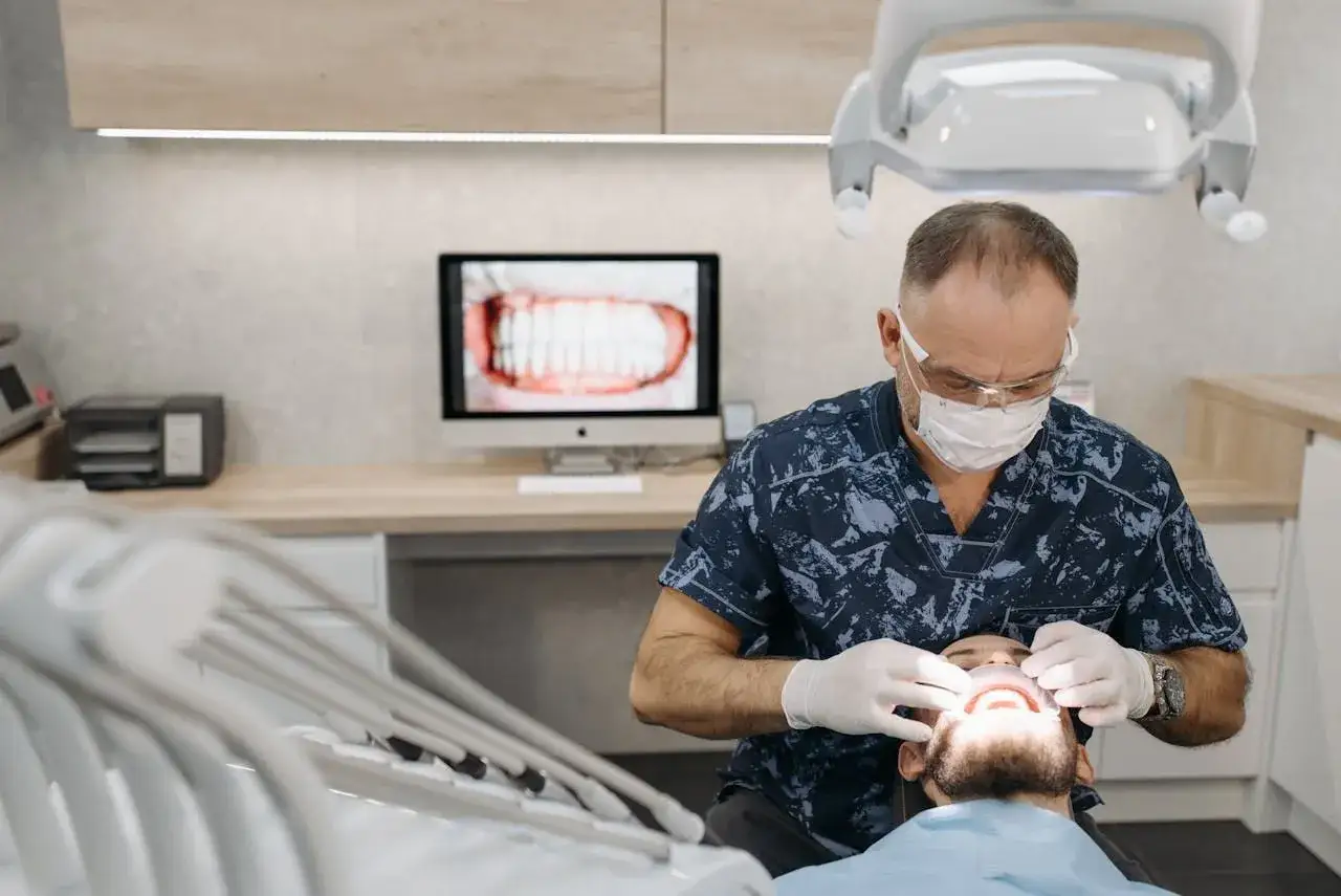 Dentysta w masce i rękawiczkach bada usta pacjenta.