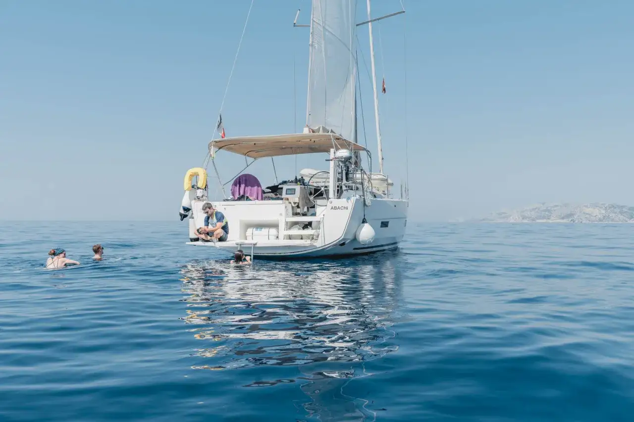 Erfahrungen, wenn du der Crew beitrittst: Ein Mann sitzt auf einer Yacht, während andere im Meer schwimmen.